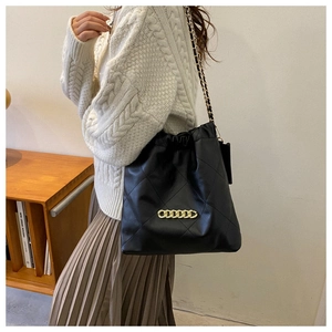 Detail of black quilted leather shoulder bag with gold chunky chain strap on a model