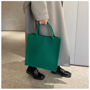 Detail of green tote bag with crocodile texture carried by model in a grey coat