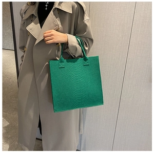 Detail of green tote bag featuring luxury crocodile texture and leather top handles