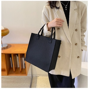 Detail of black tote bag featuring faux snake texture and elegant top handles