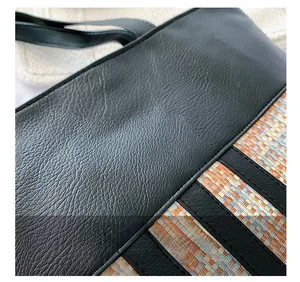 Close-up of black litchi leather bag with woven pattern fabric and precision stitching