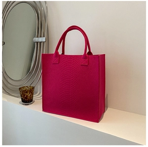 Detail of rose red felt tote bag with premium crocodile pattern texture on a white stand