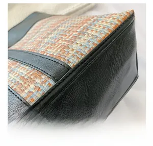 Detail shot of multicolor woven fabric and black leather stitching on a large tote bag