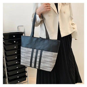 Close-up of a large tweed patchwork tote bag styled with a white blazer and black skirt