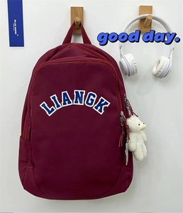 Close-up of burgundy nylon backpack featuring arc logo and plush bear charm