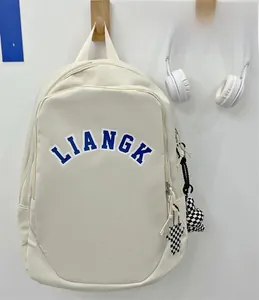 Close-up of white nylon backpack with blue lettering and checkered bear pendant charm