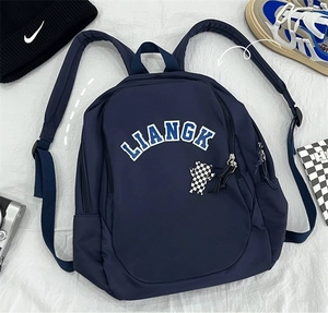 Detail of navy nylon backpack with LIANGK print and checkered bear keychain accessory