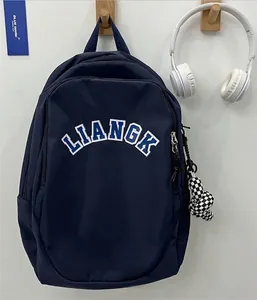 Minimalist navy blue nylon backpack with LIANGK logo and checkered charm on a wall
