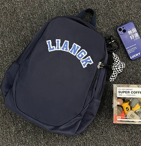 Detailed close-up of navy nylon backpack with LIANGK letter patch and bow charm