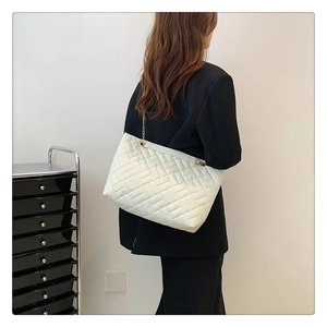 Detail of a large cream quilted tote bag with gold chain strap worn by a model