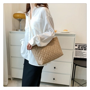 Close-up of beige quilted tote bag with golden chain strap on a model for daily style