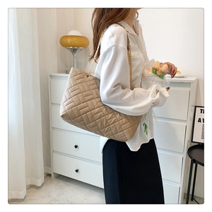 Quilted tote bag in beige leather with golden chain strap worn by a model in a minimal setting