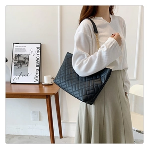 Detail of a large black quilted tote bag with chain strap on an office desk