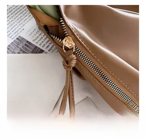 Detailed close-up of brown leather bag featuring golden metal zipper and knotted leather puller