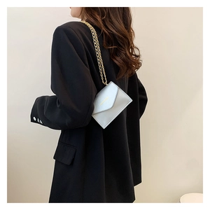 Detail view of mini white envelope chain bag with gold lettering worn on black blazer