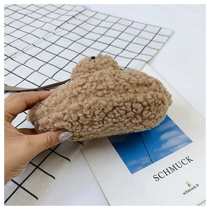 Détail du petit sac bandoulière en peluche ours brun doux tenu sur un fond à carreaux