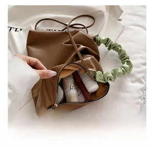 Detail of coffee pleated handbag showing spacious interior with cosmetics and green handle