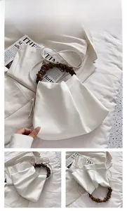 Detail of white cloud bucket bag featuring brown ruched handle and slim shoulder strap
