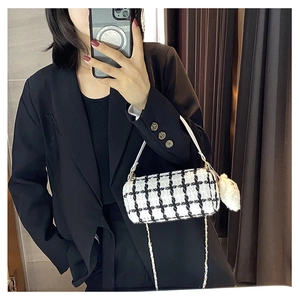 Detail of tweed checkered cylindrical bag with white leather strap and plush charm accent