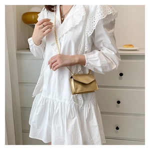 Close-up of a stylish gold chain mini bag on a white dress with elegant triangle flap