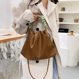 Minimalist brown ruched bucket bag with green handle shown on a model in neutral tones