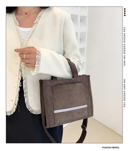 Detail of a brown corduroy tote bag featuring a large pocket and stylish white stripes
