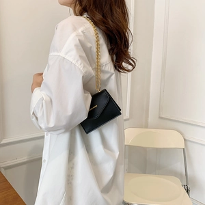 Fashionable black mini flap bag with gold chain strap shown in a lifestyle interior