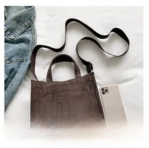 Detail view of brown corduroy handbag with gray reflective strip and adjustable shoulder strap