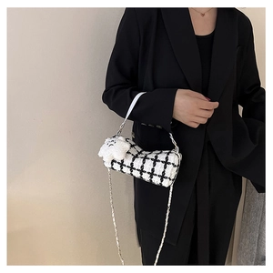 Checkered tweed cylinder bag with white handle and plush dog charm worn by model