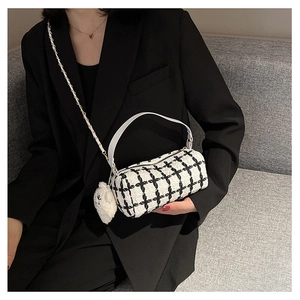 Close-up of black and white checkered tweed barrel bag with plush bear charm detail