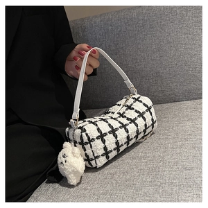 Detail of tweed checkered cylindrical bag with white leather strap and plush charm