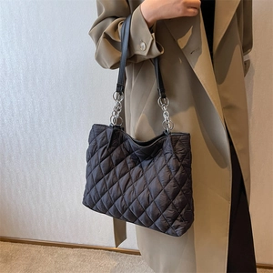 Minimalist black quilted nylon tote bag with silver chain strap shown on a model