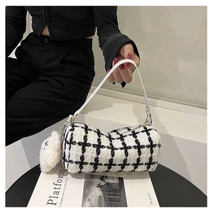 Detail of tweed checkered cylindrical bag with white leather handle and plush bear charm