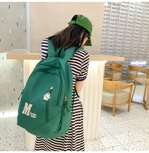 Detail of green nylon backpack with zipper side pocket and white bear pendant decoration