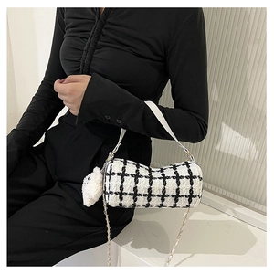 Detail of tweed barrel bag featuring black and white plaid pattern and plush charm