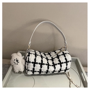 Detail of checkered tweed cylinder bag with leather handle and cute plush bear charm