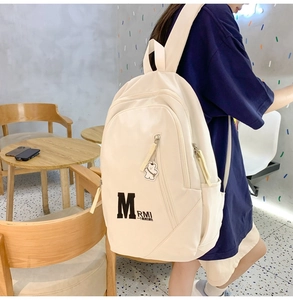 Detail view of the beige student backpack with M logo and cute bear pendant on a model