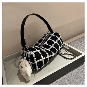 Detail view of black and white checkered tweed cylinder bag with cute white bear plush charm