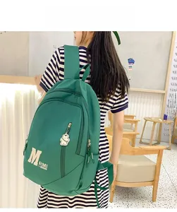 Detail of dark green nylon backpack with white lettering and a cute bear charm accessory