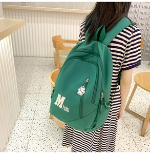 Detail view of large green nylon backpack featuring a cute bear keychain and letter prints