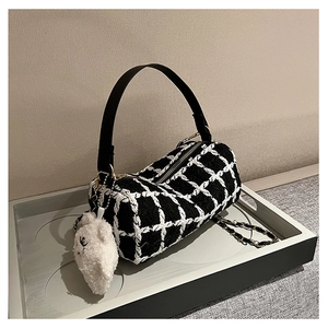Detail view of cylinder plaid handbag featuring black and white tweed with a plush bear charm