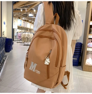Close-up of brown nylon backpack featuring white lettering and a cute bear keychain accessory
