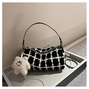 Detail of a black and white tweed cylinder bag with a golden chain and teddy bear charm