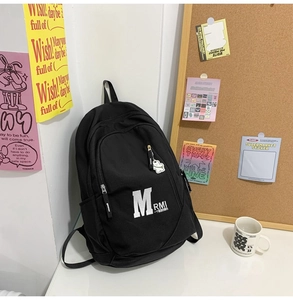 Detail of a large black canvas backpack featuring a side cartoon pendant in a school setting