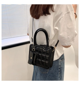Detail of black quilted shoulder bag featuring round handles and a detachable coin purse