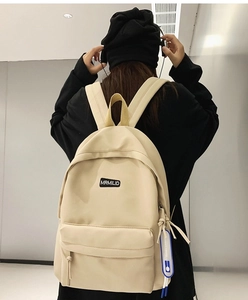 Back view of a student wearing a minimalist beige waterproof nylon backpack with logo