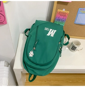 Close-up of green canvas backpack with white letter print and cute bear keychain detail