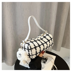 Close-up of black and white tweed cylinder bag with cute plush bear charm and gold chain