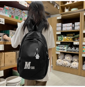 Close-up of black retro school backpack featuring a bear pendant and white letter print