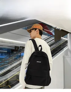 Side view of black canvas backpack on male model showing padded straps and logo